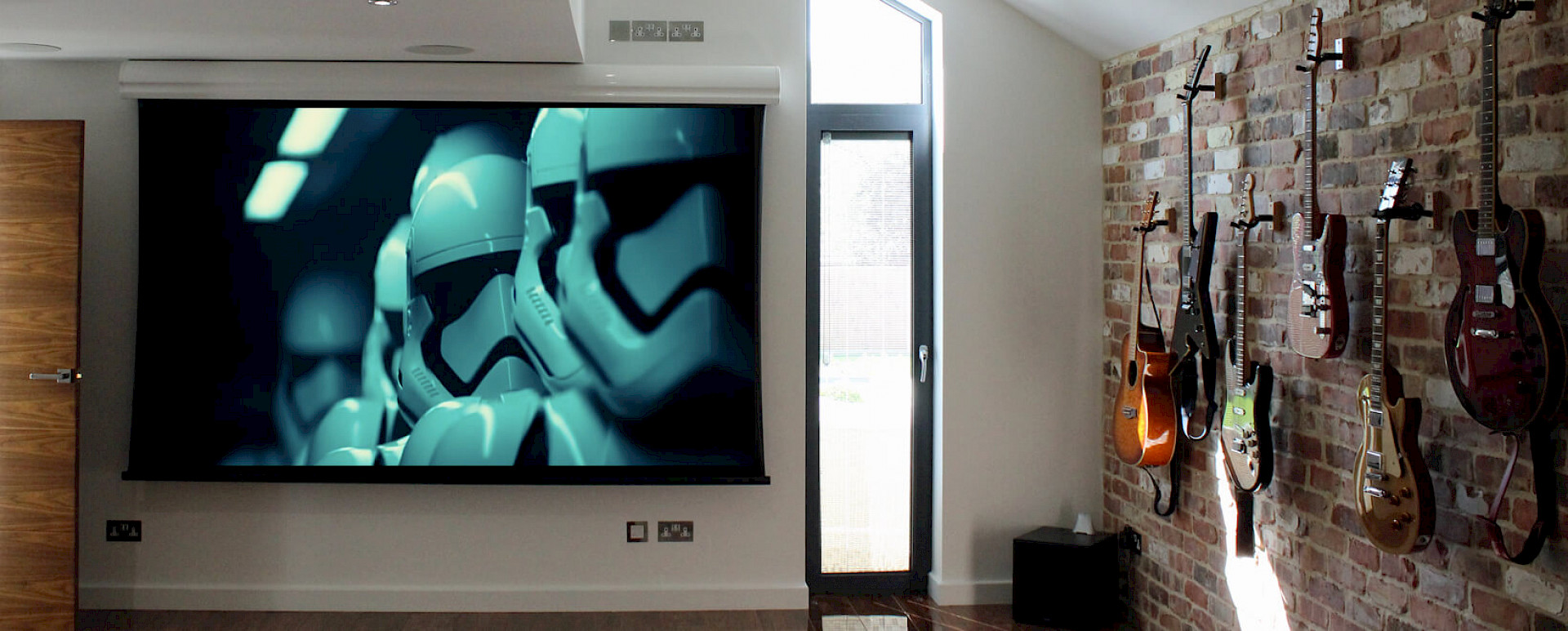 Home cinema projector screen in a room, the wall on the left is full of guitars being displayed